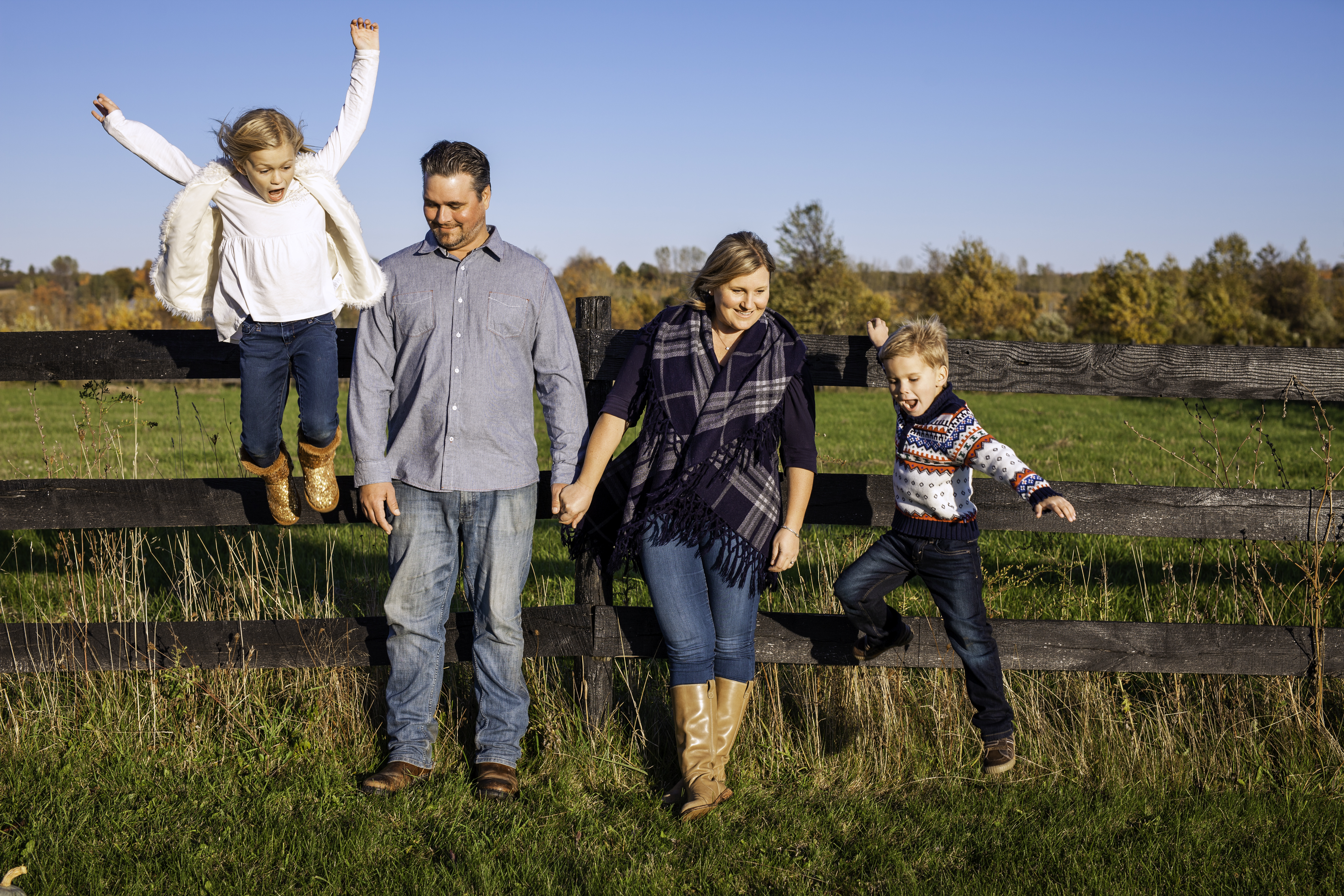 Kids jumping off of a fence and parents smiling