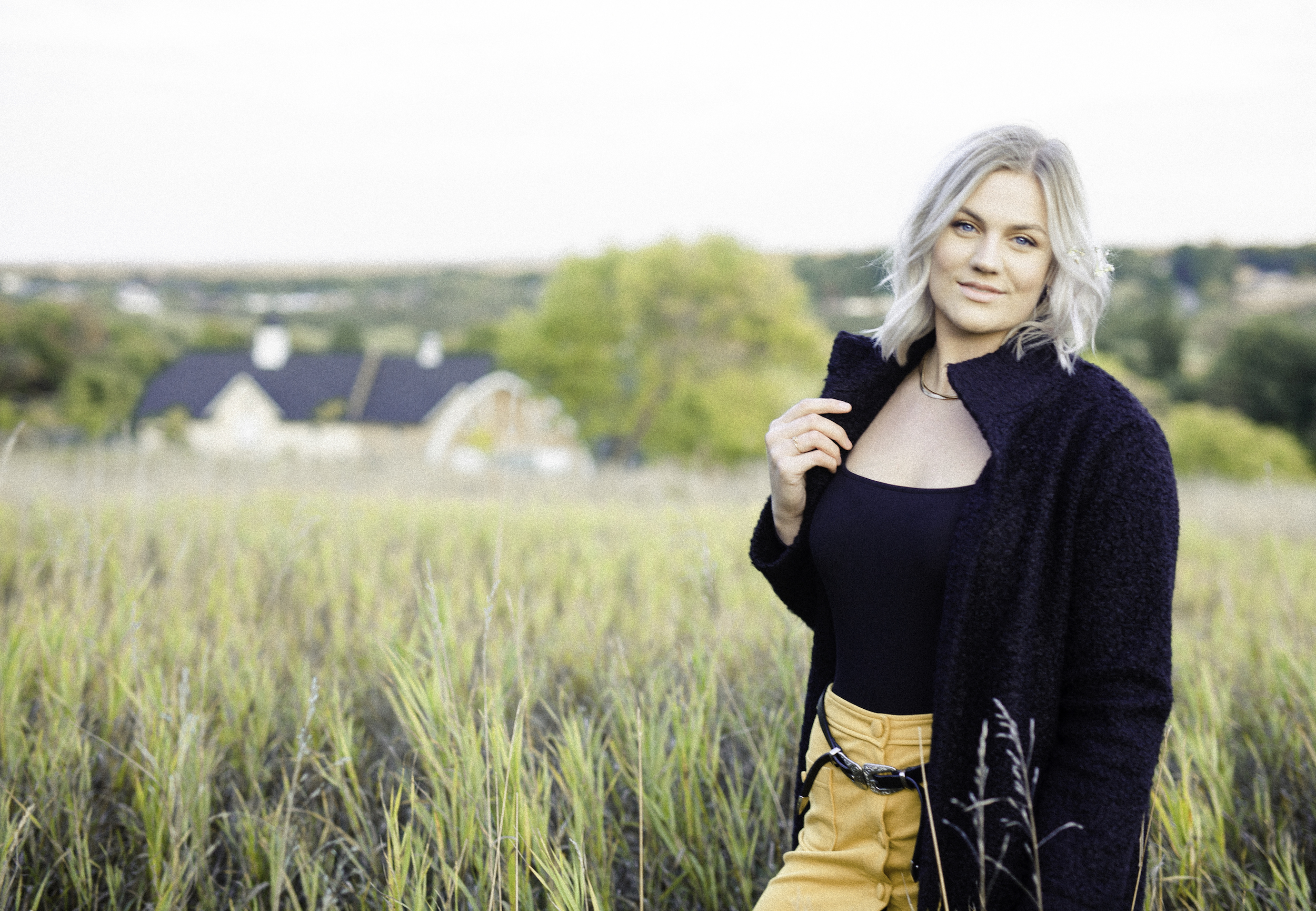 J holding coat collar, standing in a field