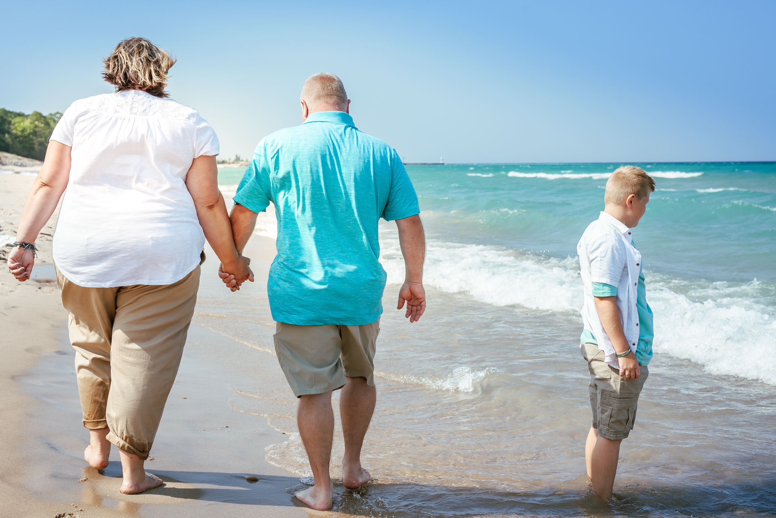 Couple holding hands walking on the beach with child wading nearby
