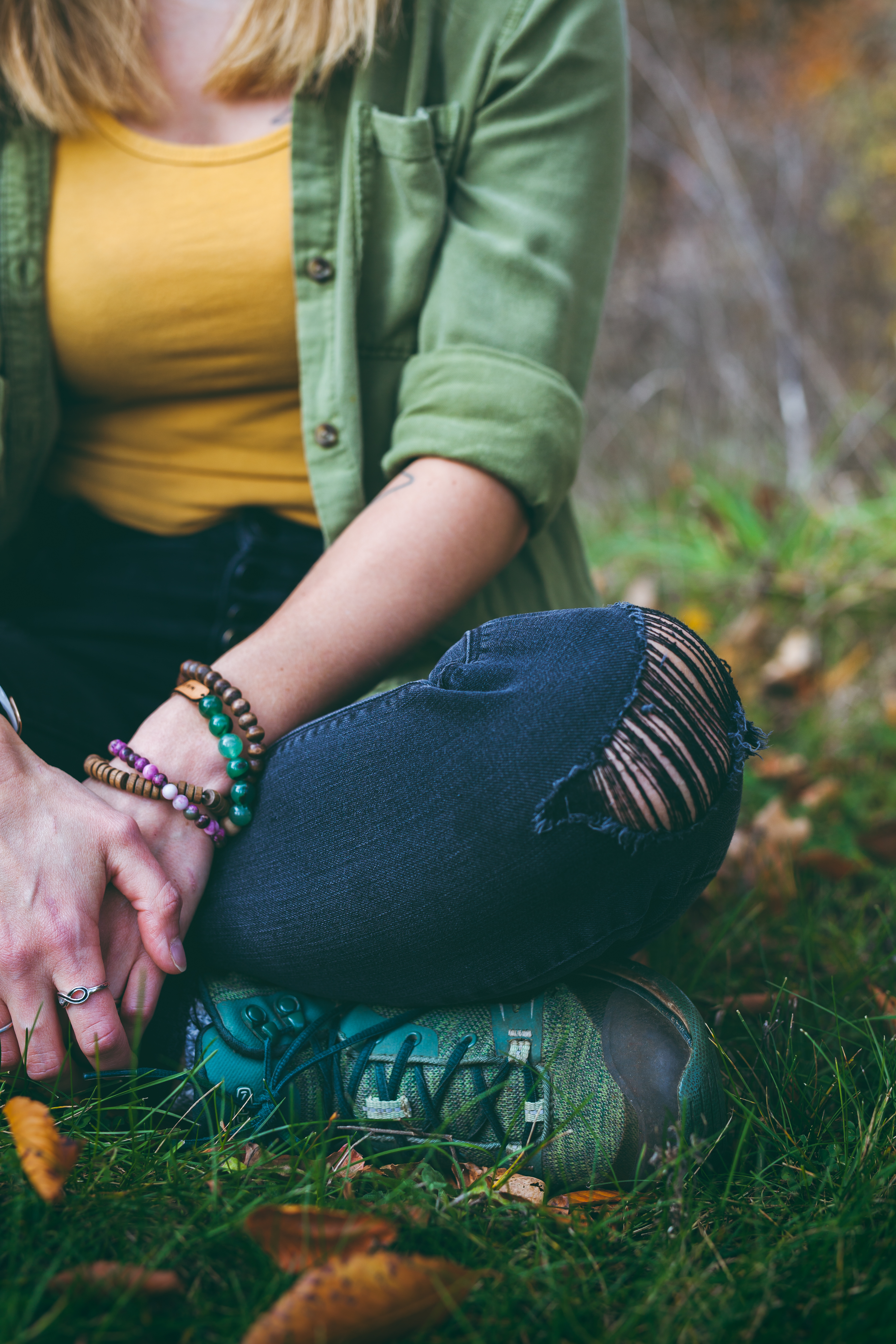 Detail of ripped knee in jeans, bracelets, and green shoe of woman